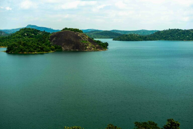 Peisaj al unui lac calm din Abuja, Nigeria, cu dealuri și natură luxuriantă.
