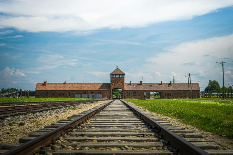 Poarta principală Auschwitz-Birkenau cu liniile de cale ferată sub cer senin.