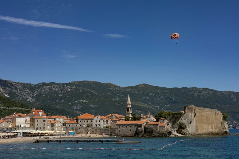 The historic Budva old town and its walls, with a beach and mountain scenery in the background.