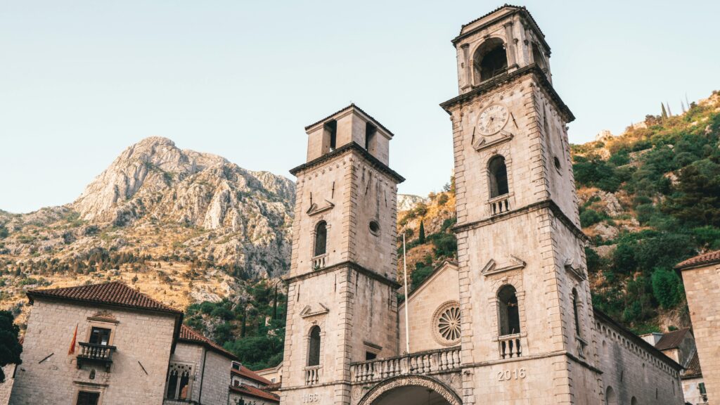Catedrala Sfântul Trifon din Kotor cu turnuri gemene înconjurată de peisaj montan.