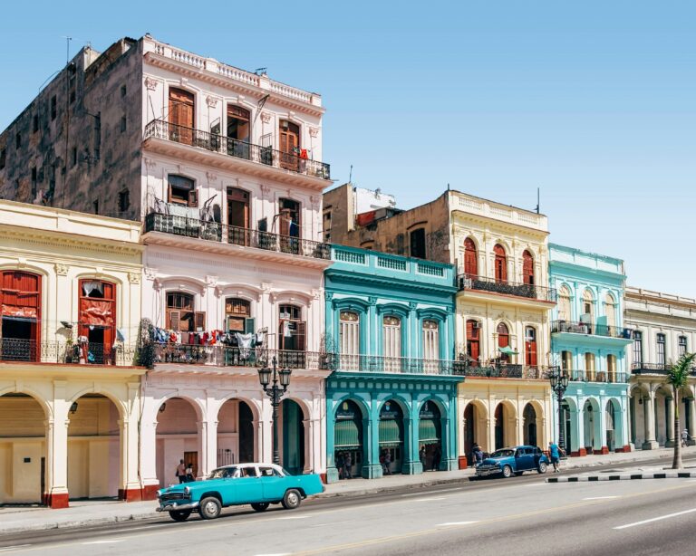Clădiri coloniale colorate și o mașină clasică albastră pe o stradă din Havana