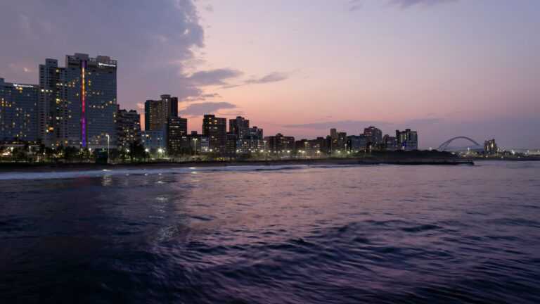 Durban city skyline with illuminated buildings and ocean at sunset.