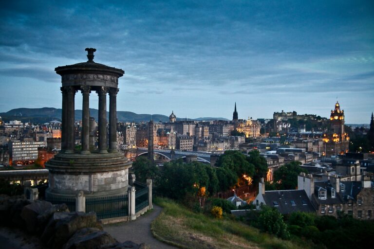 Panoramic view of Edinburgh at night with the Dugald Stewart Monument in the foreground and the city in the background.