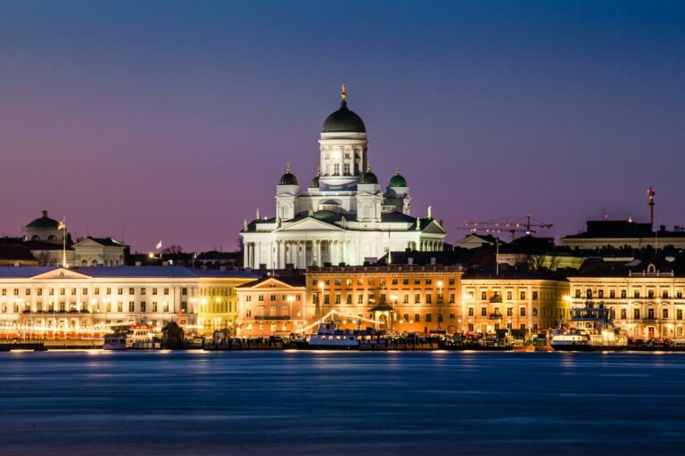 Catedrala Helsinki iluminată noaptea cu clădiri înconjurătoare și cerul violet portocaliu în Finlanda.