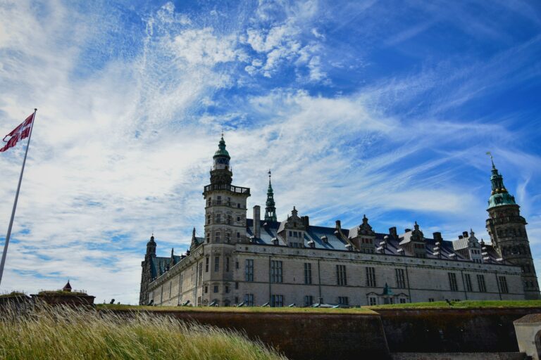 Kronborg Castle in Helsingor, Denmark, seen with a clear blue sky and the Danish flag waving.