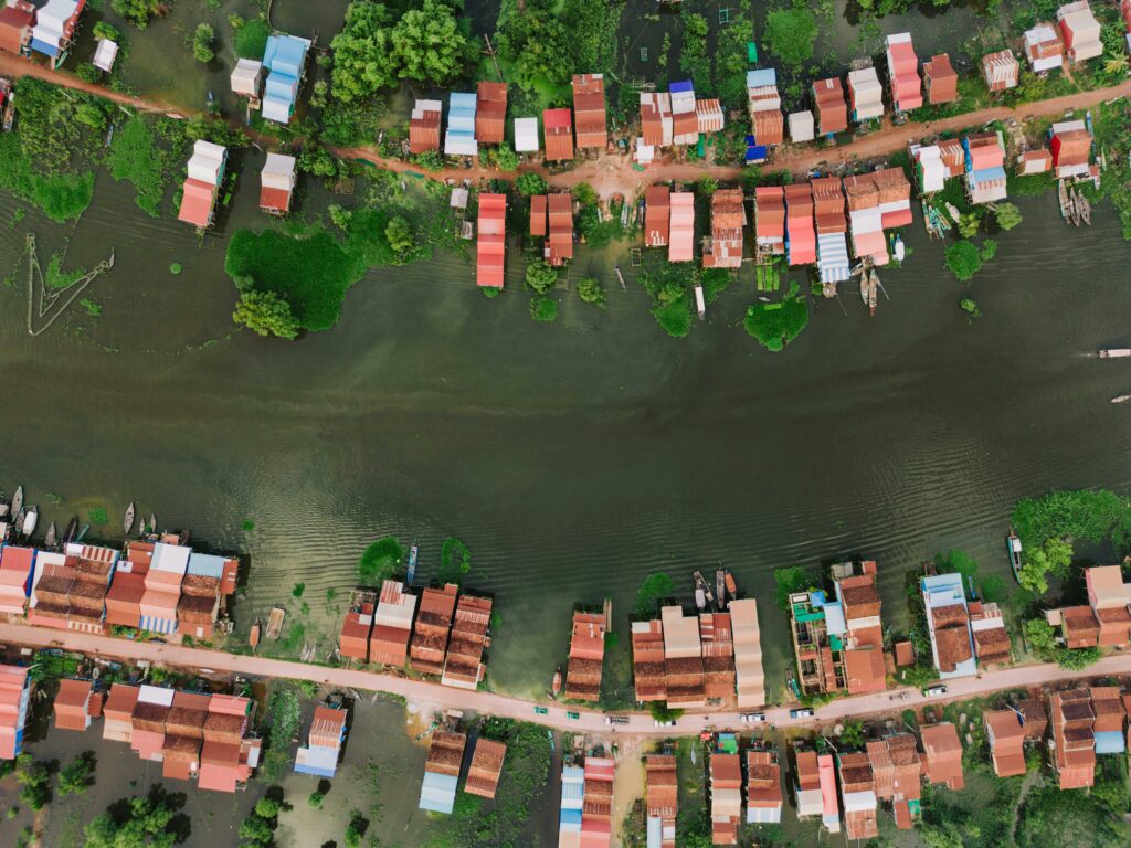 Vedere aeriană a satului plutitor de pe Tonlé Sap Lake, cu case colorate, apă liniștită și vegetație verde.