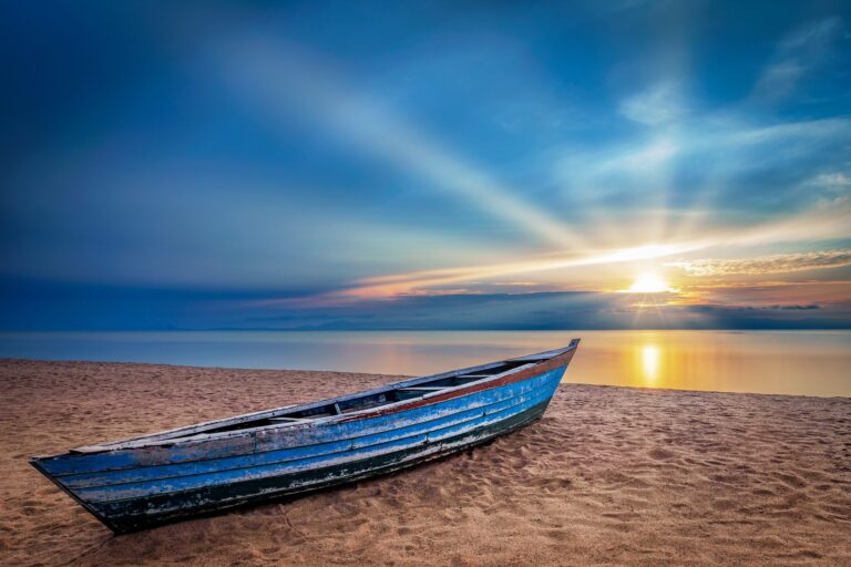 Apus de soare pe Lacul Malawi cu o barcă albastră tradițională pe nisip.