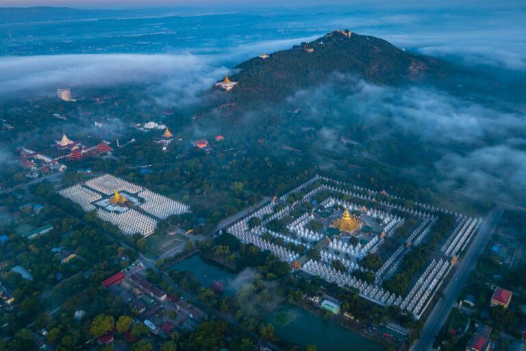 Mandalay pagoda aerial view with surrounding hills and greenery under morning mist.