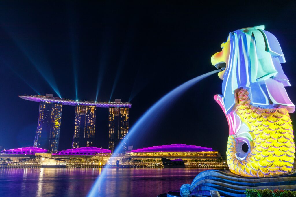 Merlion iluminat noaptea la Merlion Park, Singapore, cu Marina Bay Sands în fundal.