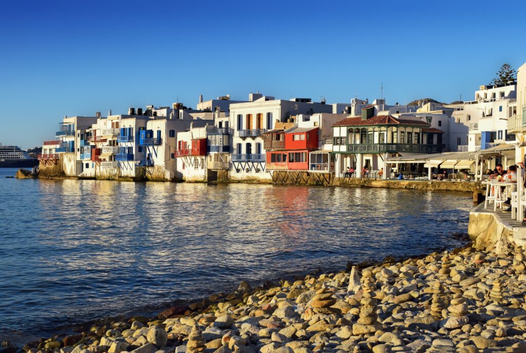 Peisaj din Little Venice, Mykonos, cu clădiri colorate și marea reflectând lumina apusului.