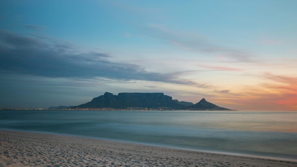 Table Mountain din Cape Town iluminat de culorile apusului, cu plajă în prim-plan.