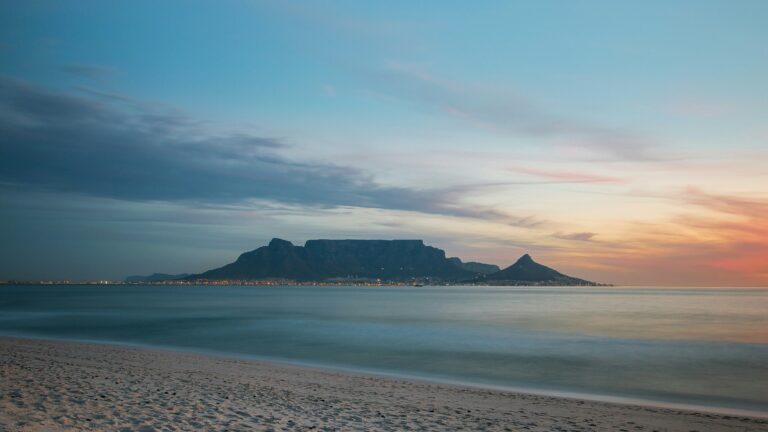 Table Mountain din Cape Town iluminat de culorile apusului, cu plajă în prim-plan.