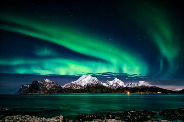 Aurora boreală deasupra munților și apelor din Norvegia.