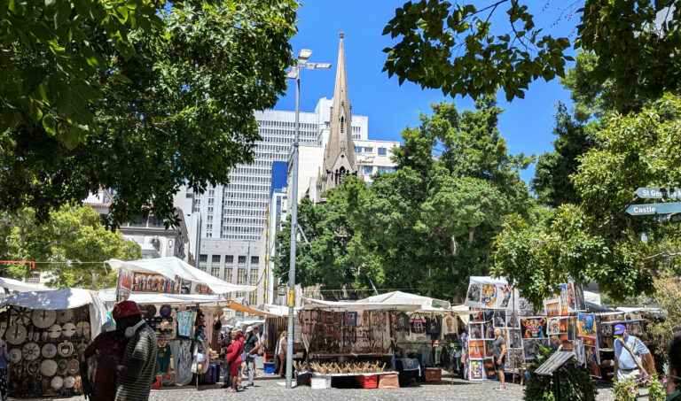 Greenmarket Square din Cape Town, cu tarabe pline de obiecte artizanale și clădiri istorice în fundal.