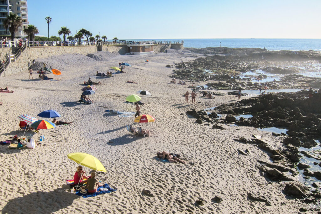 Plaja Camps Bay, Cape Town, cu umbrele colorate și nisip alb, loc popular pentru turiști.
