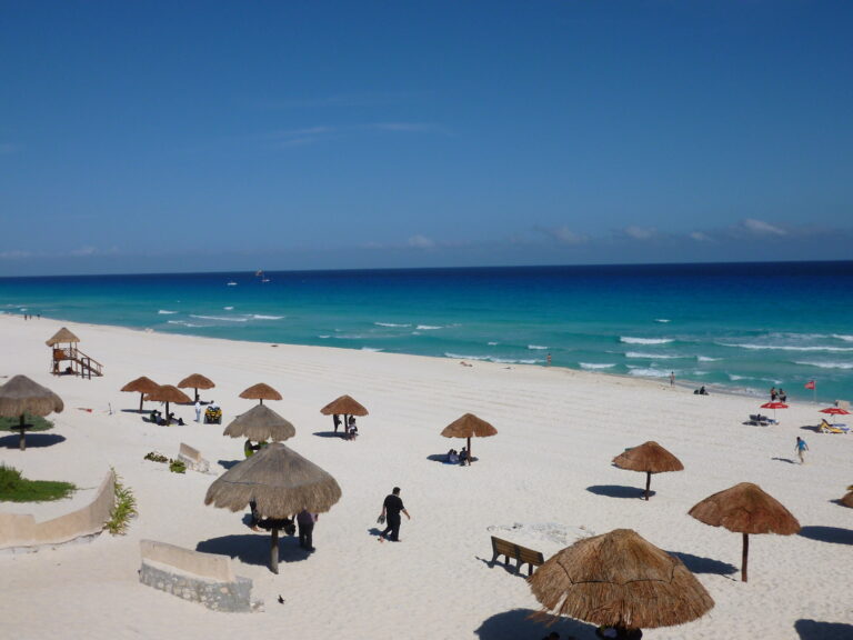 Playa Delfines din Cancun, plajă cu nisip alb și umbrele de stuf, ocean turquoise în fundal.