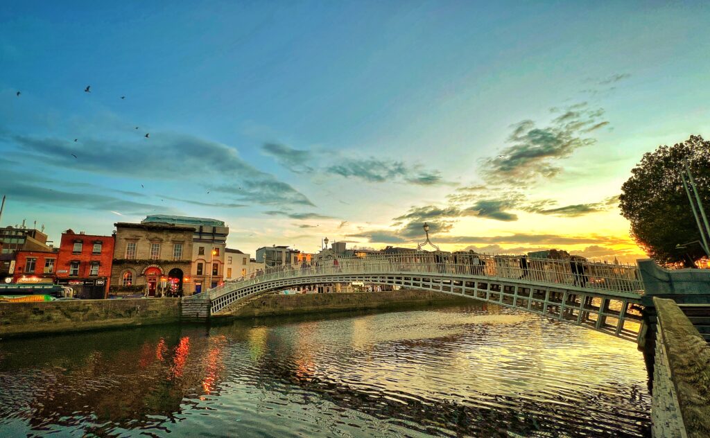 Ha'penny Bridge la apus de soare în Dublin, cu un cer colorat și reflecțiile podului în râul Liffey.