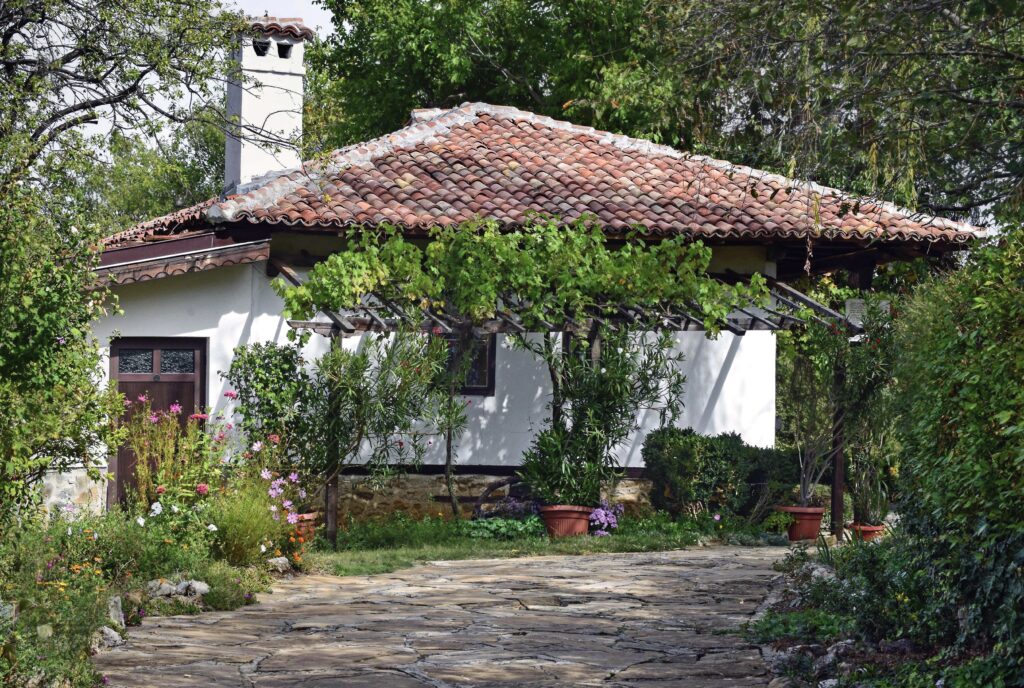 Casă tradițională din satul Arbanasi, Veliko Tarnovo, Bulgaria, înconjurată de grădini pline de flori.