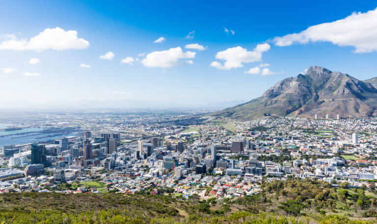 Imaginea arată orașul Cape Town și Signal Hill, cu munți pitorești și cer albastru clar, priveliște ideală pentru vizitatori.