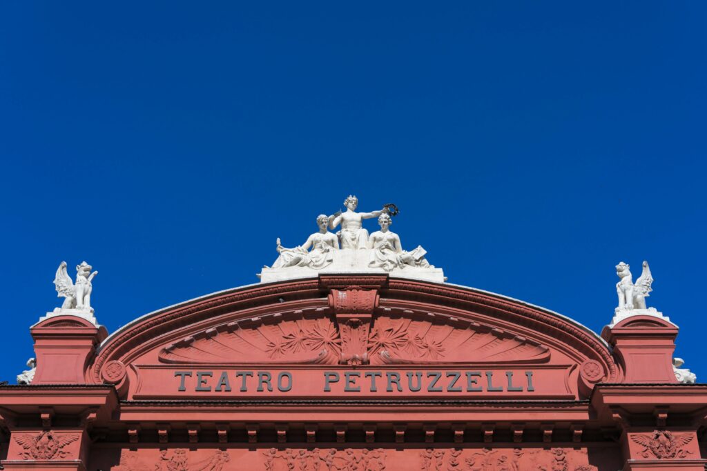 Imagine prezintă fațada Teatro Petruzzelli din Bari, Italia, cu detalii arhitecturale și statuare distincte.