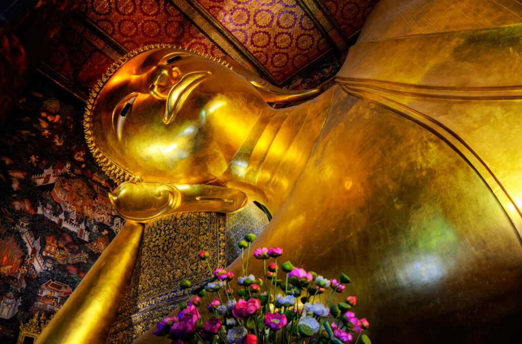 Statuia lui Buddha Culcat în Wat Pho, Bangkok, luminată și vibrantă, cu detalii intricate de aur și decor tradițional.