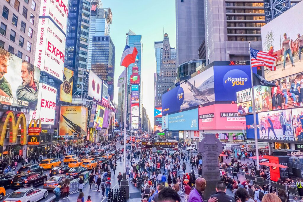 Times Square din New York, cu reclame luminoase, taxiuri galbene și mulțimi de oameni.
