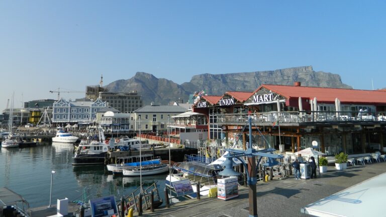 V&A Waterfront din Cape Town, cu clădiri colorate, bărci și Table Mountain pe fundal.