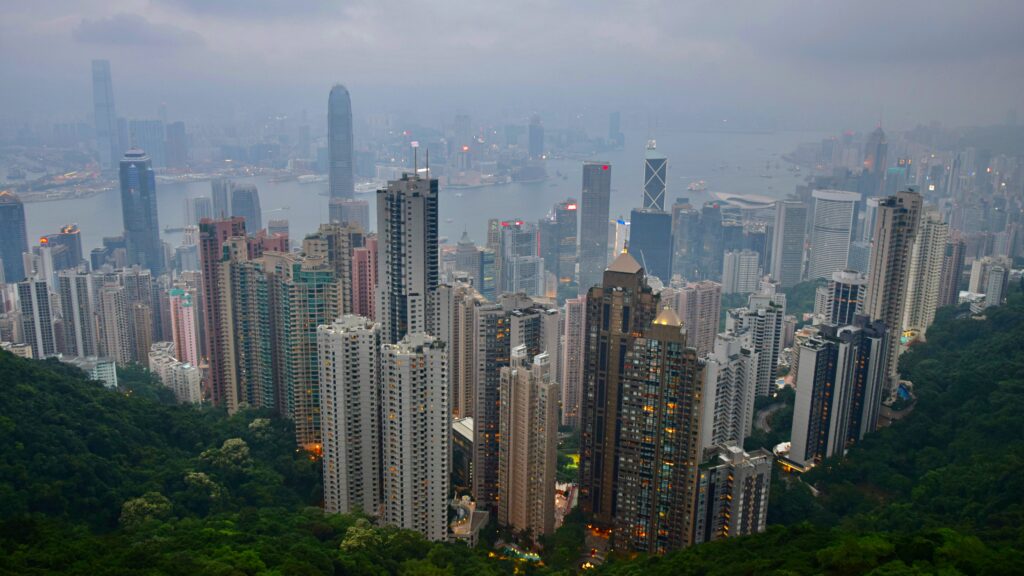 Priveliște panoramică de la Victoria Peak, Hong Kong, în amurg, cu clădiri înalte și golful în fundal.