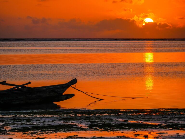 Sunset in Zanzibar with a traditional African boat along the ocean shore.