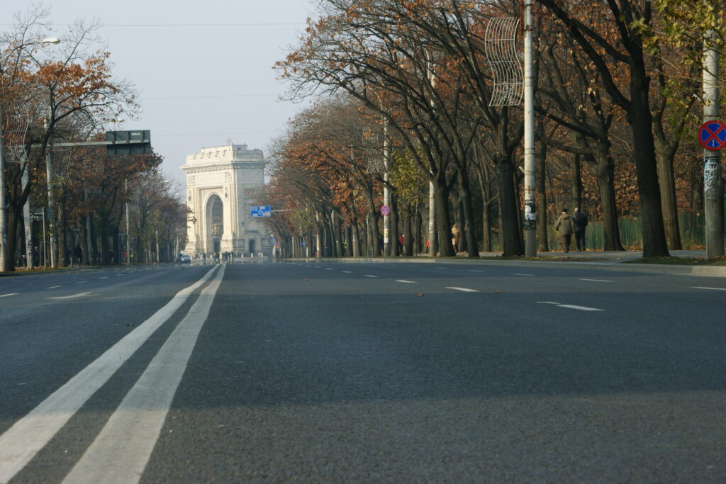 Arco di Trionfo di Bucarest visto da un ampio viale, circondato da alberi d'autunno.