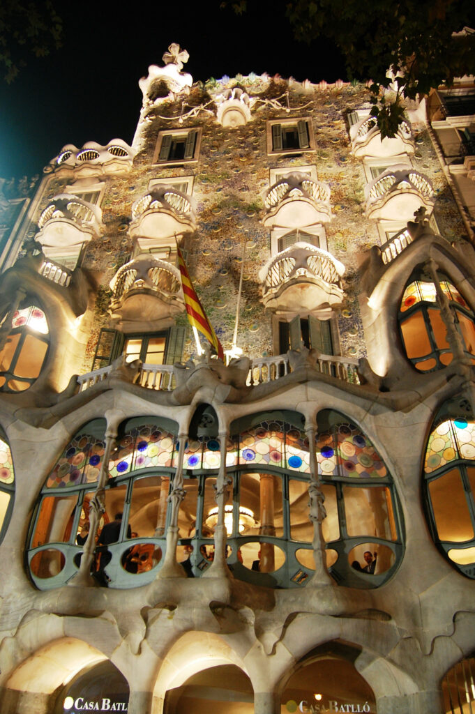 Fațada iluminată a Casei Batlló din Barcelona noaptea, evidențiază detaliile arhitecturale unice.