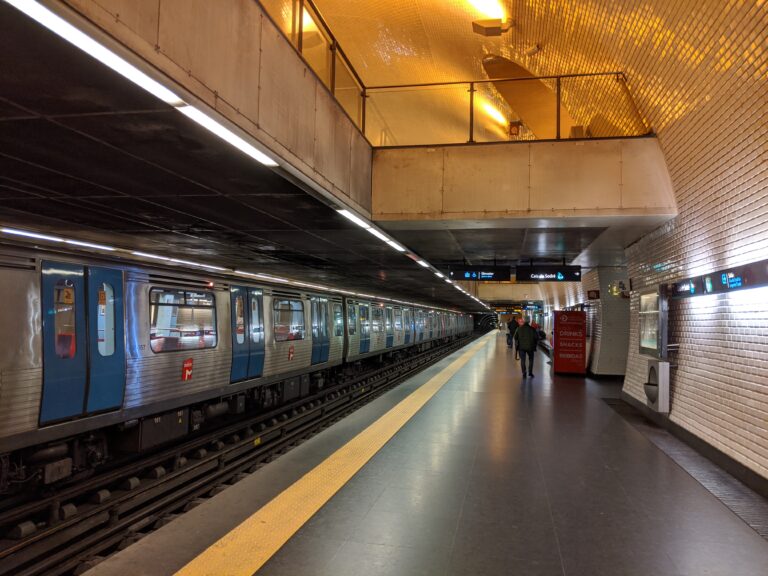 Stazione della metropolitana Baixa-Chiado a Lisbona con treni e passeggeri sulla piattaforma.