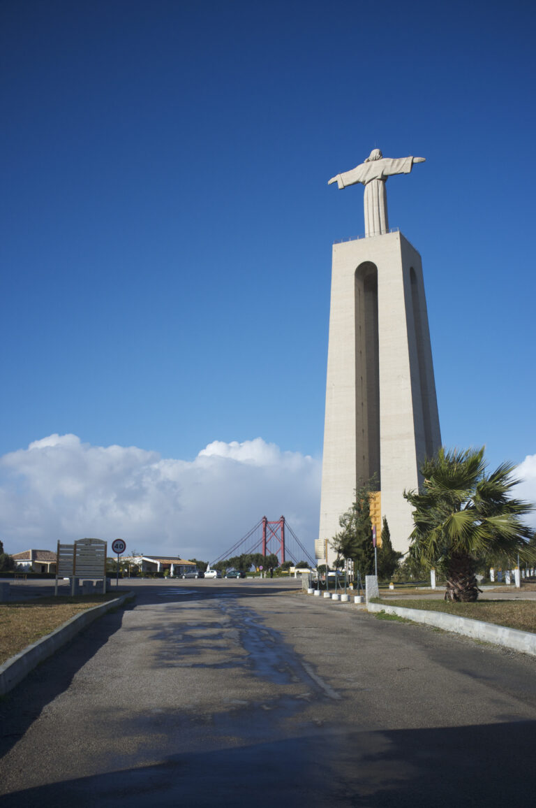 Cristo Rei a Lisbona, statua alta su un piedistallo con il Ponte 25 aprile sullo sfondo.