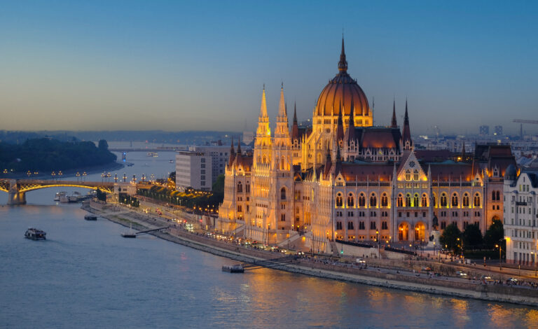 Parlamentul din Budapesta iluminat noaptea, vedere panoramică pe Dunăre cu nave turistice.