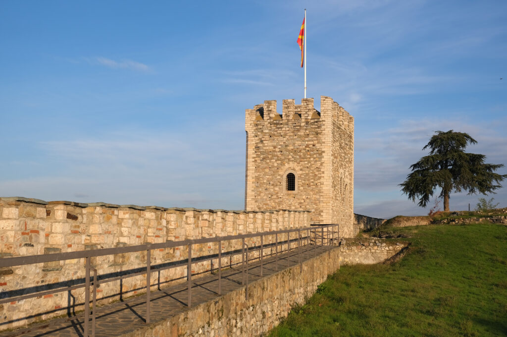 Torre storica con bandiera macedone alla Fortezza Kale di Skopje, circondata da un paesaggio verde.