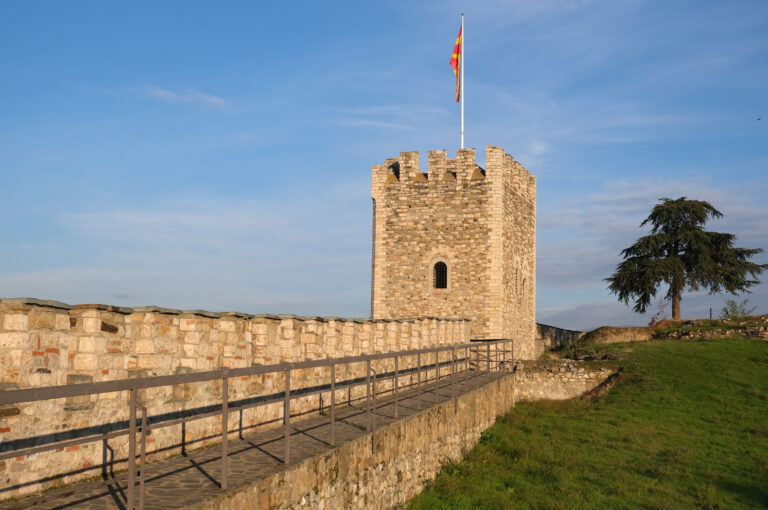 Torre storica con bandiera macedone alla Fortezza Kale di Skopje, circondata da un paesaggio verde.