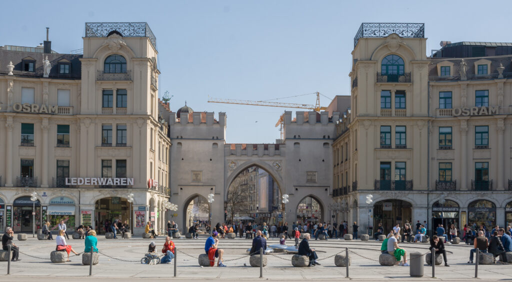 Karlsplatz Stachus a Monaco di Baviera con edifici storici e persone che si rilassano nella piazza.