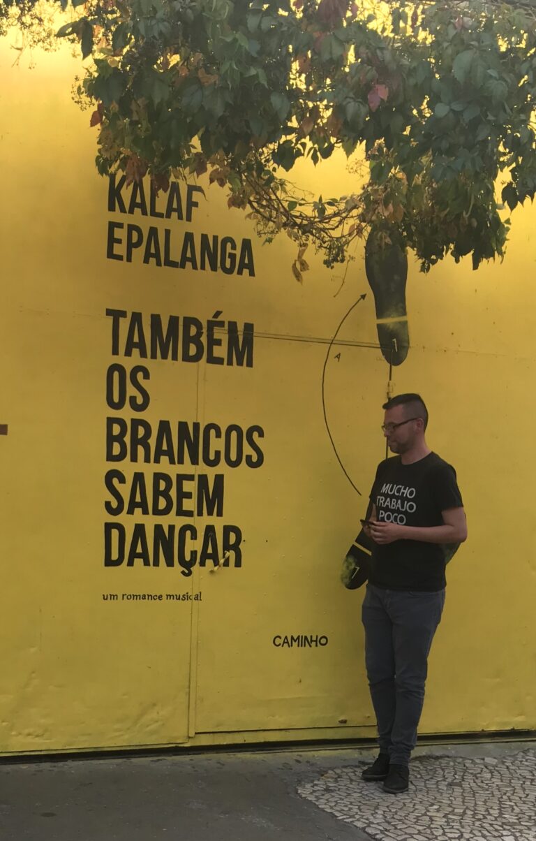 Arte urbana a LX Factory Lisbona, muro giallo con iscrizioni vibranti.