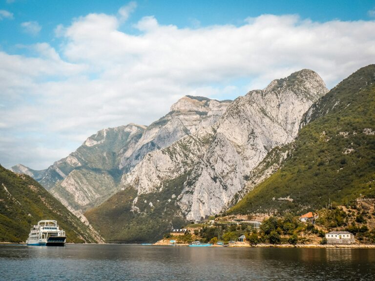 Lacul Komani din Shkoder, Albania, cu vapor turistic și munți spectaculoși în fundal.