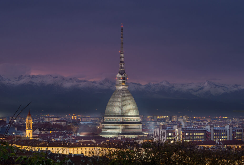 Immagine della Mole Antonelliana, simbolo iconico di Torino, illuminata al tramonto con le Alpi sullo sfondo.
