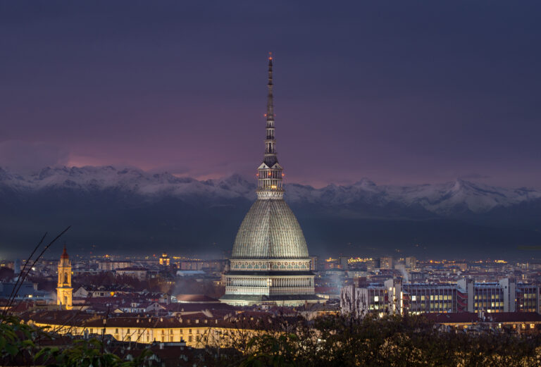 Immagine della Mole Antonelliana, simbolo iconico di Torino, illuminata al tramonto con le Alpi sullo sfondo.