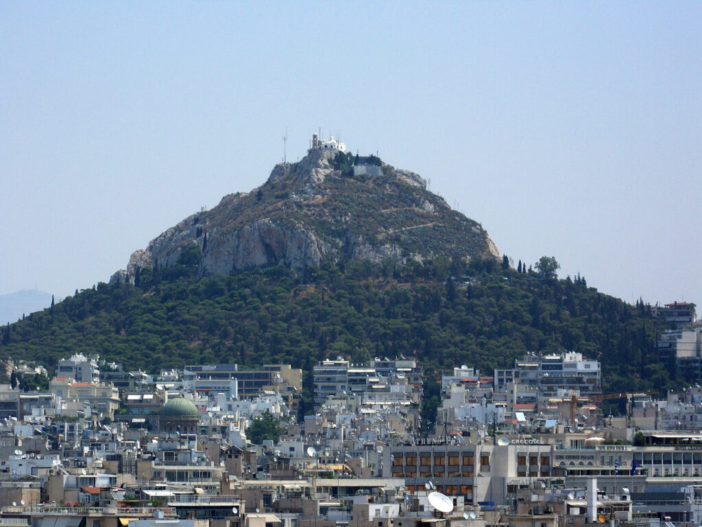 Vista del Monte Lycabettus ad Atene, una collina circondata da vegetazione e edifici moderni.