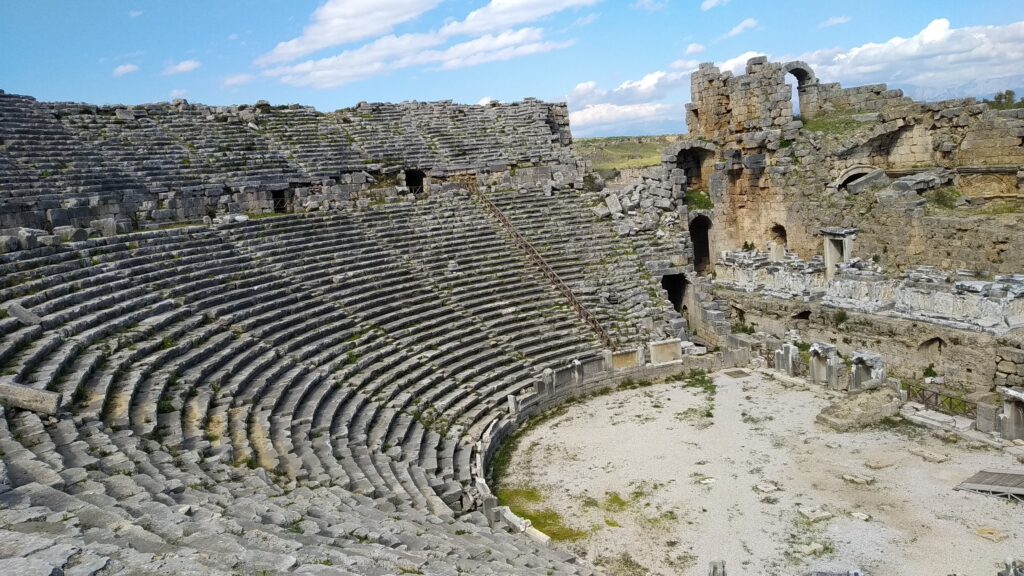 Foto del teatro antico di Perge, Antalya, con sedili in pietra e strutture storiche.