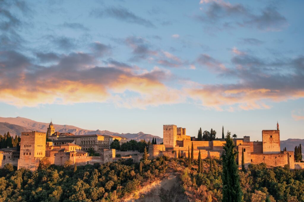 Imagine a Palatului Alhambra la apus, cu cer colorat și arhitectura impresionantă în Granada.