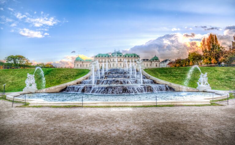 Palatul Belvedere din Viena iluminat la apus, cu fântâni spectaculoase în prim-plan.