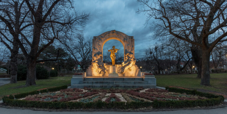 Monumento a Johann Strauss, dorato e situato nel Stadtpark di Vienna, circondato da un paesaggio notturno e alberi.