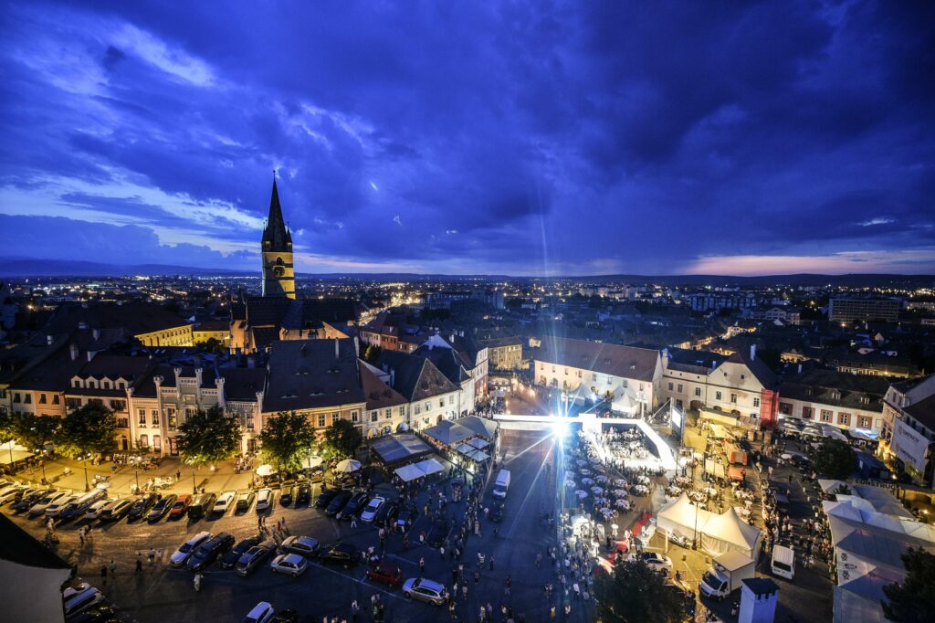 Piața Mică di Sibiu al tramonto con edifici storici e luci serali.