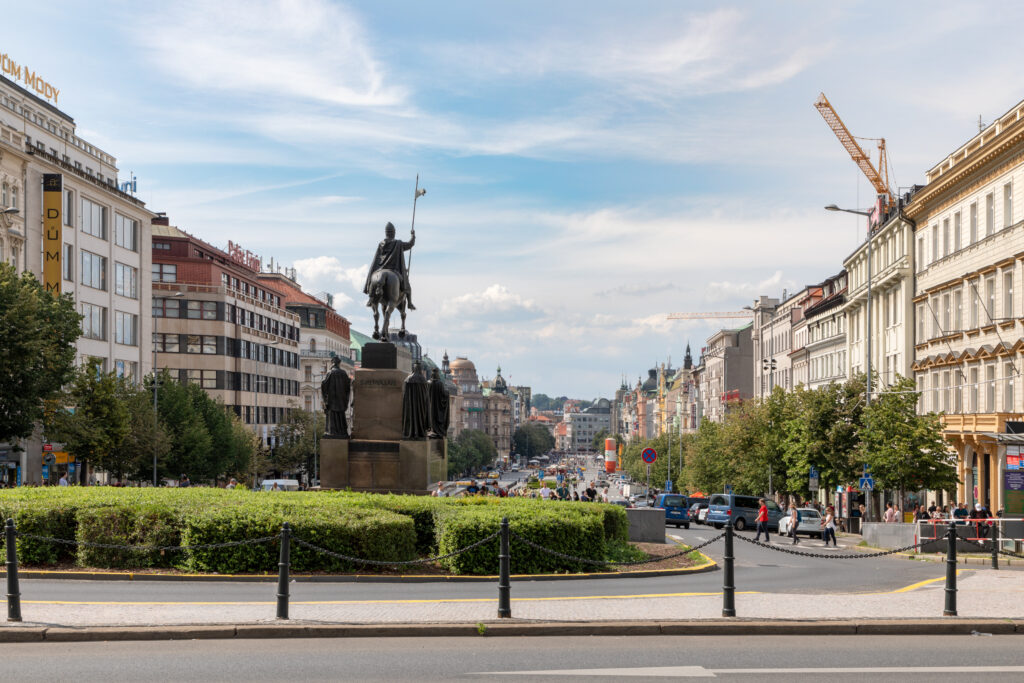 Statuia Sf. Václav din Piața Wenceslas, înconjurată de clădiri istorice și peisaj urban din Praga.