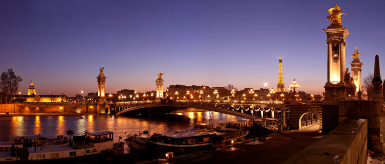 Ponte Alexandre III al tramonto con illuminazione spettacolare e Torre Eiffel visibile.