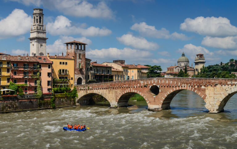 Ponte Pietra a Verona con atmosfera soleggiata e edifici storici, fiume Adige che scorre sotto.